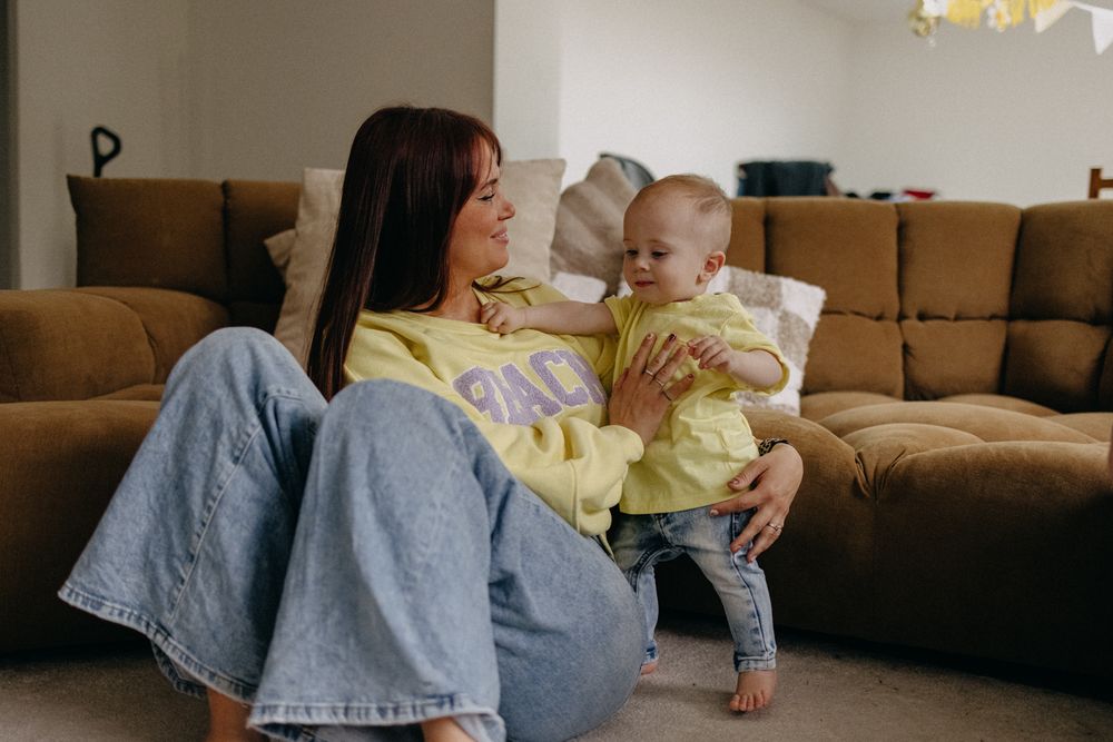 Two people in casual yellow and denim outfits share a tender moment while relaxing on a brown couch at home.