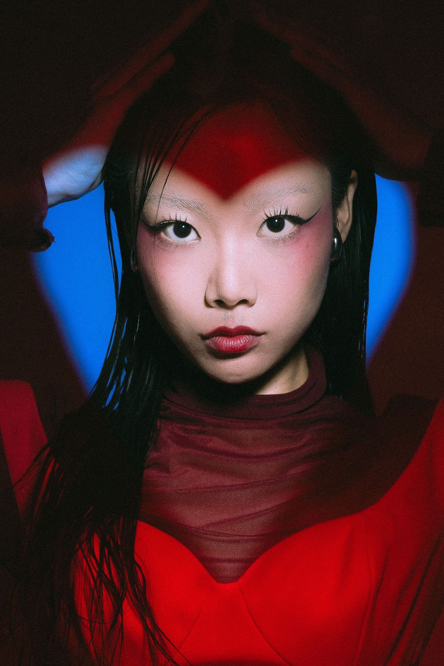 Dramatic portrait with red and blue lighting creates striking contrast against dark hair and red turtleneck top.