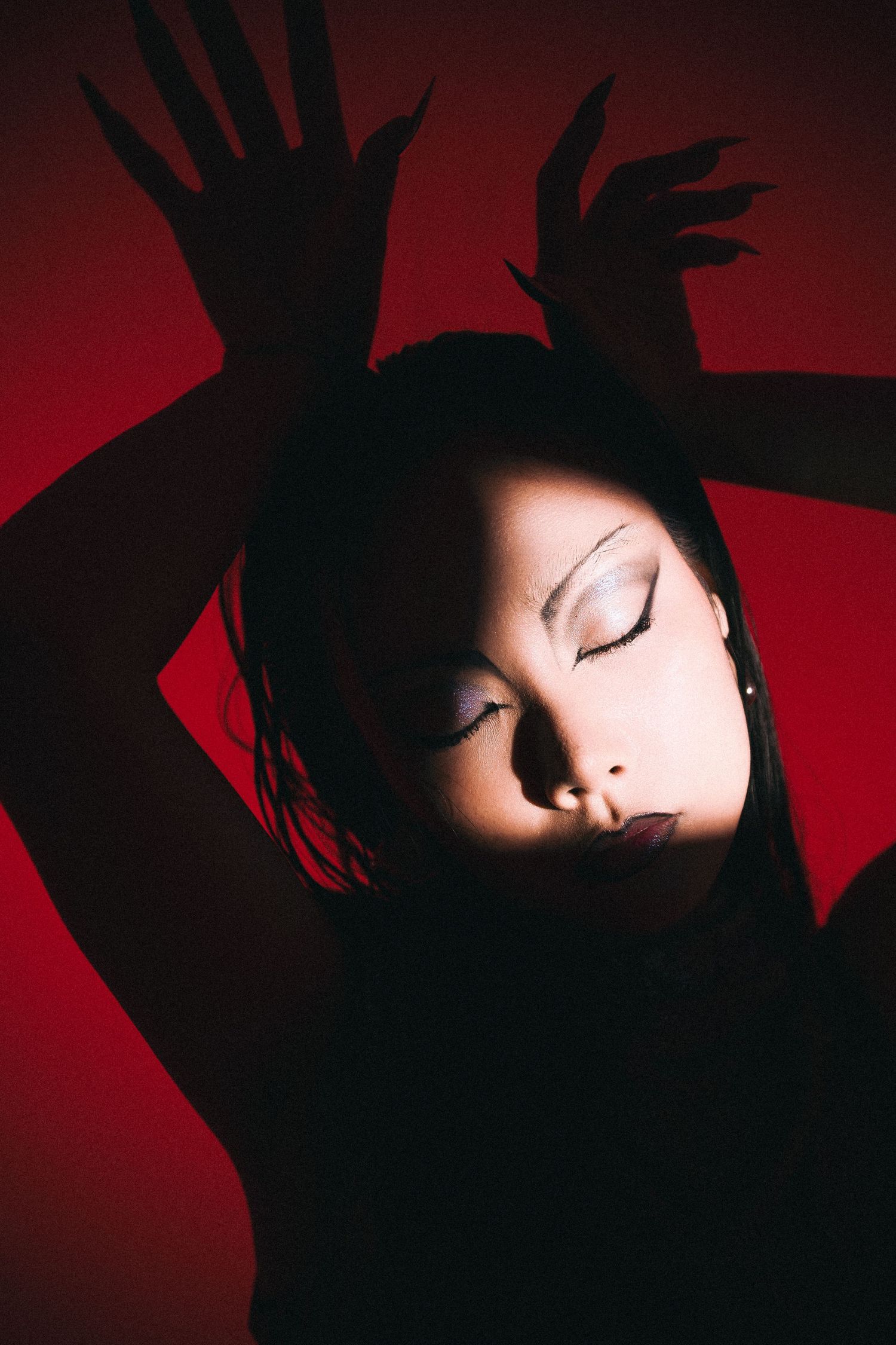 Dramatic artistic portrait against red background with shadowy hands creating stark silhouettes and contrast.