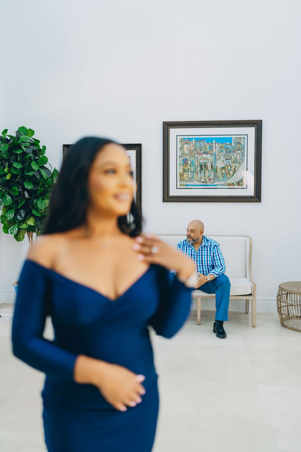 A person in a navy blue fitted dress stands in an elegant white room with decorative wall art and greenery.