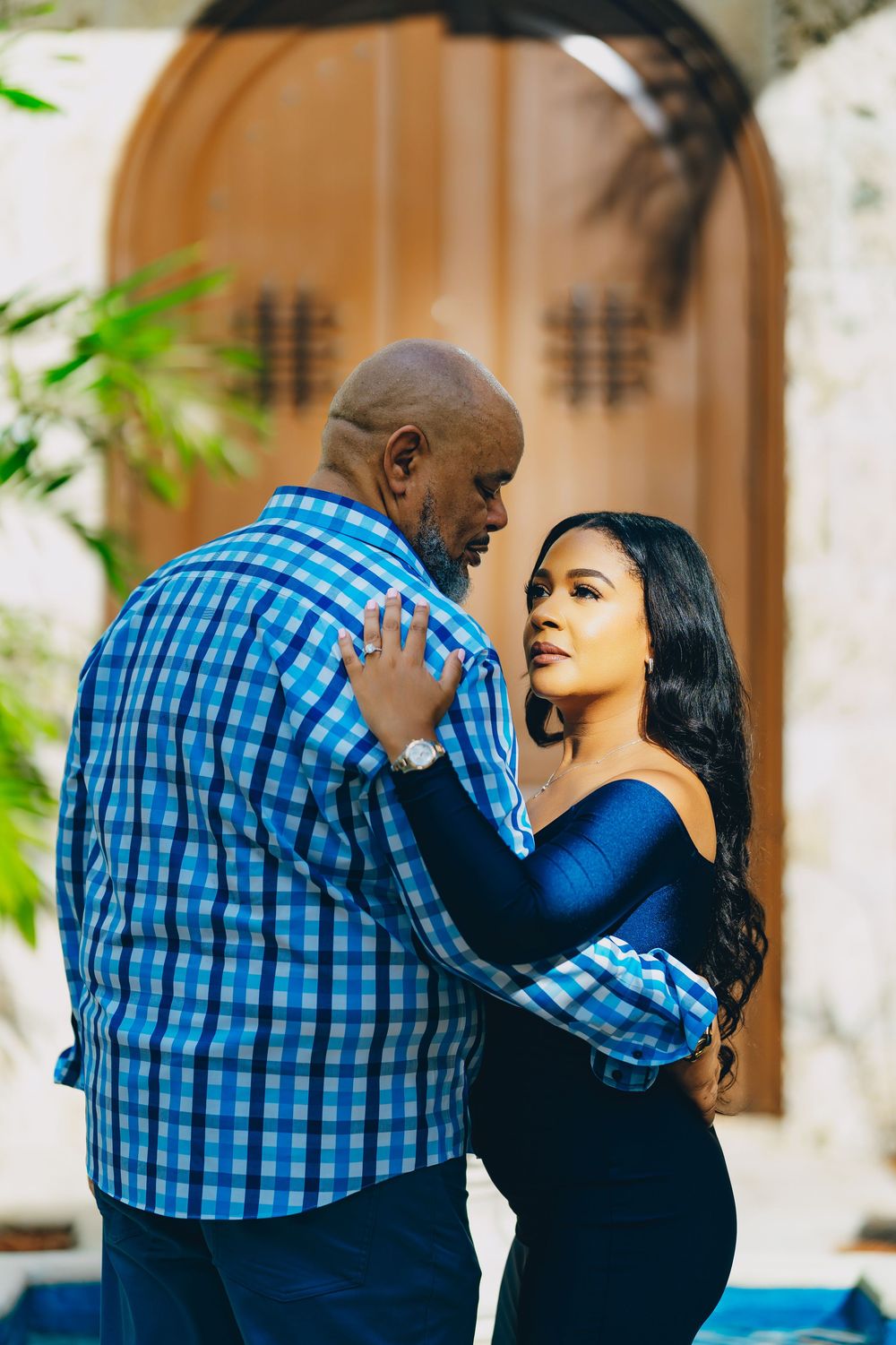 A romantic couple in coordinating blue outfits embrace while dancing together beside an arched wooden door.