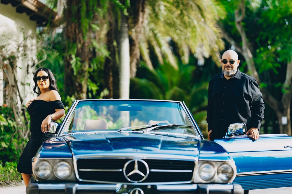 A vintage blue Mercedes-Benz convertible car parked in front of palm trees on a sunny day.