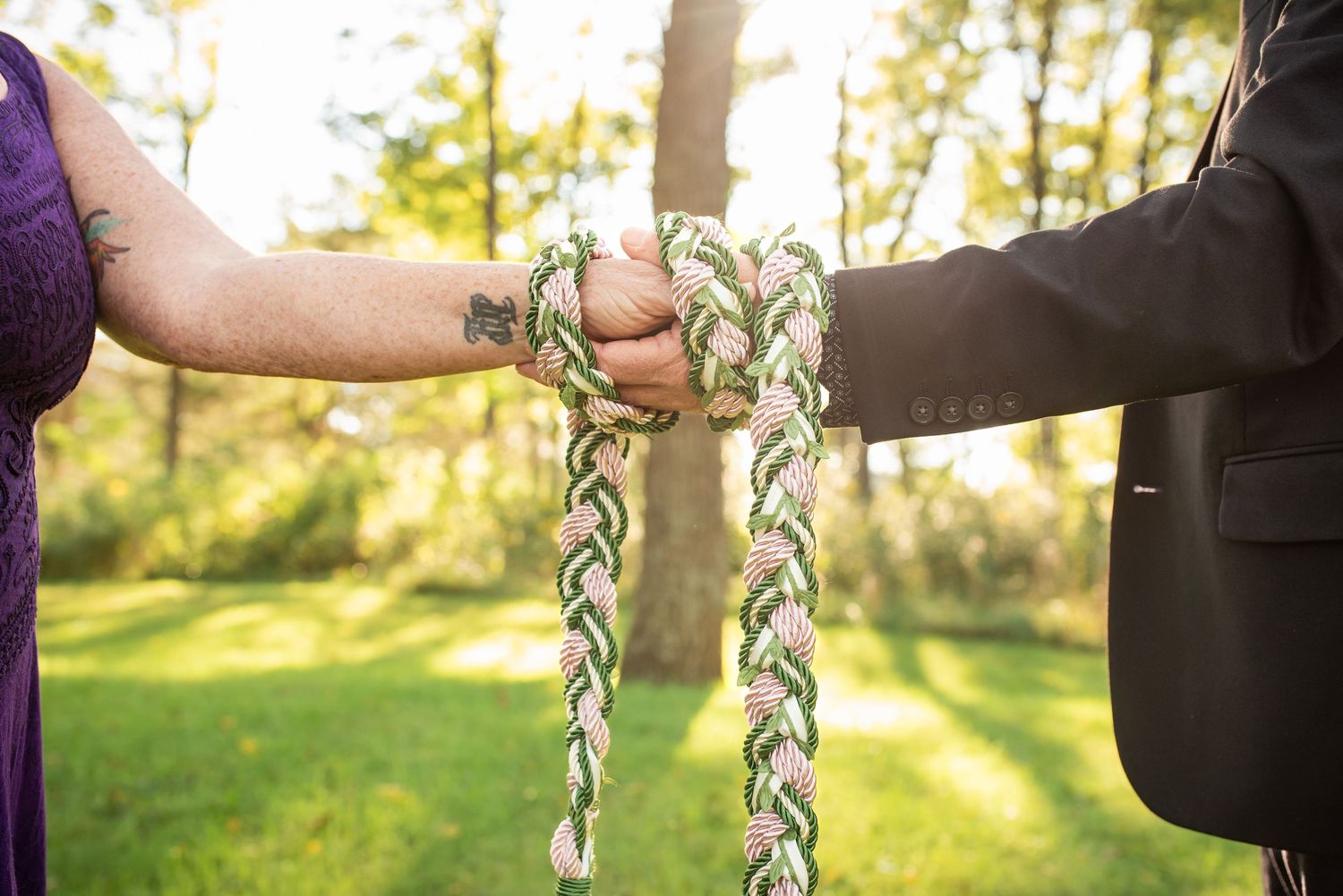 Hands hold decorative braided cord during outdoor ceremony ritual.