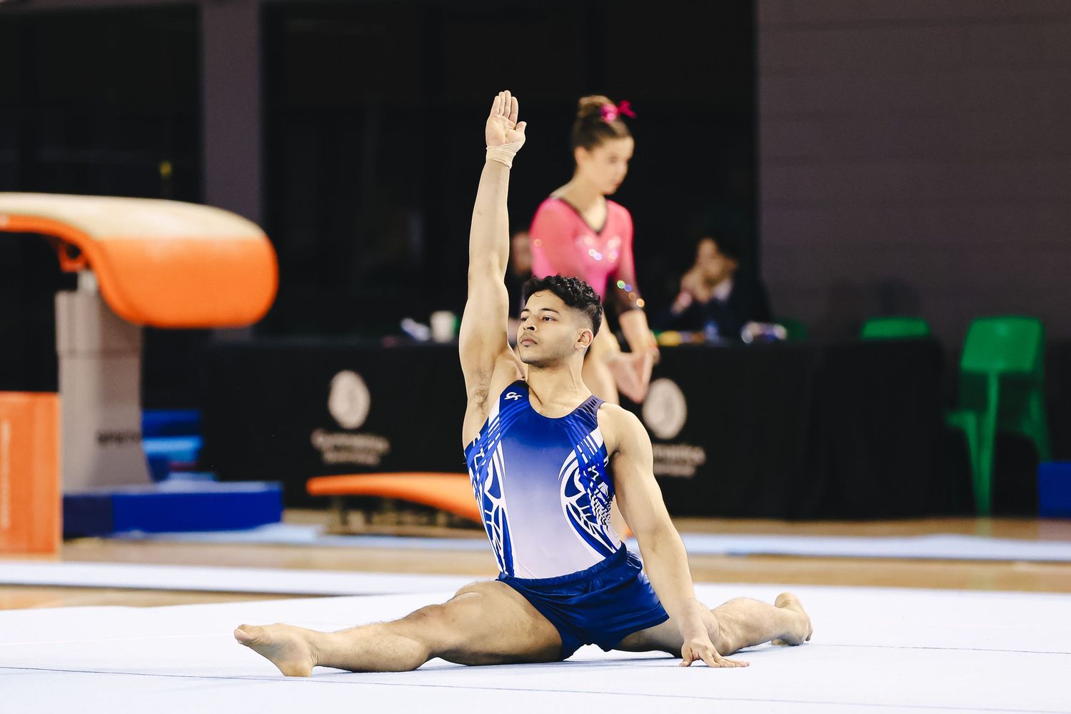 Young gymnast in blue leotard performs a backbend during floor exercise routine at indoor competition.