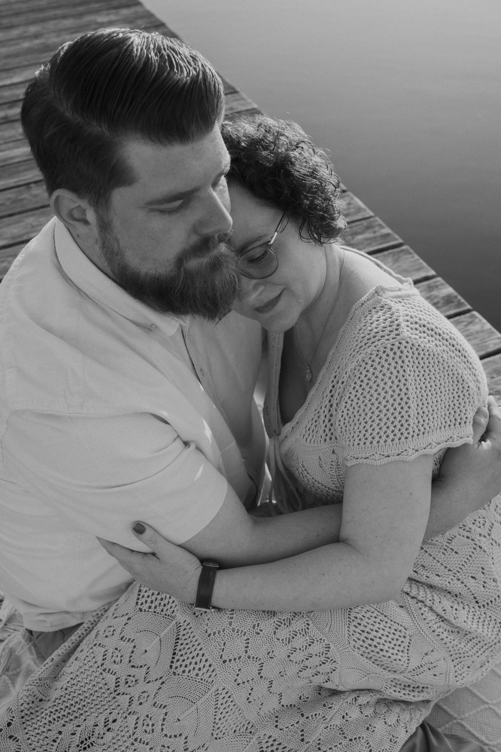 A romantic black and white portrait of a couple sharing an intimate moment on a wooden dock.
