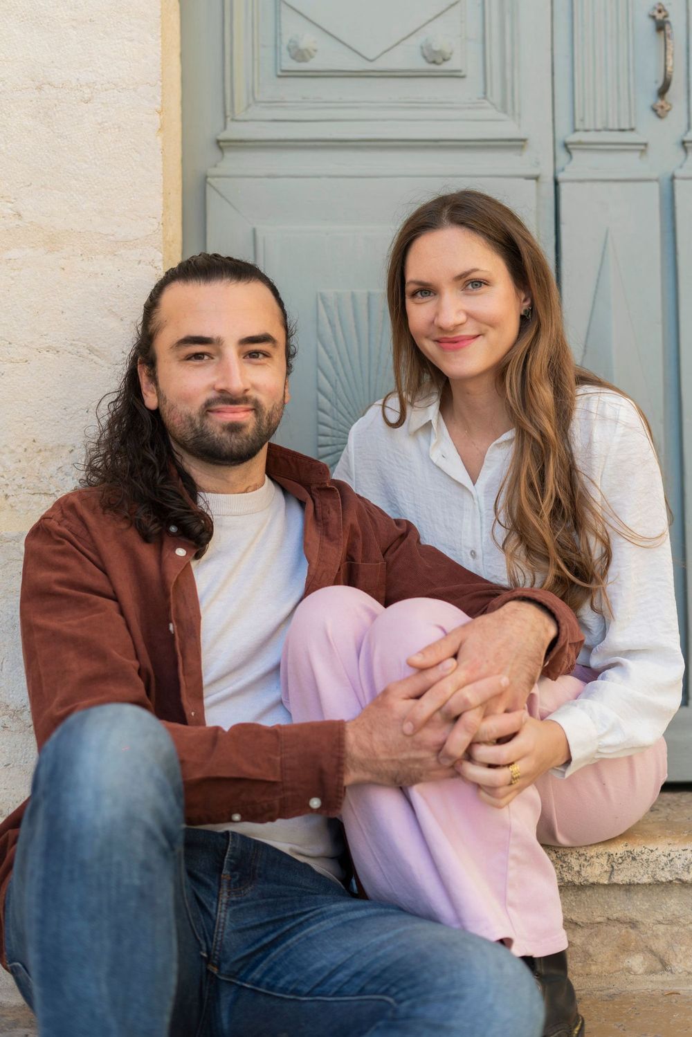 Casually dressed couple sitting together on stone steps in front of a blue door.
