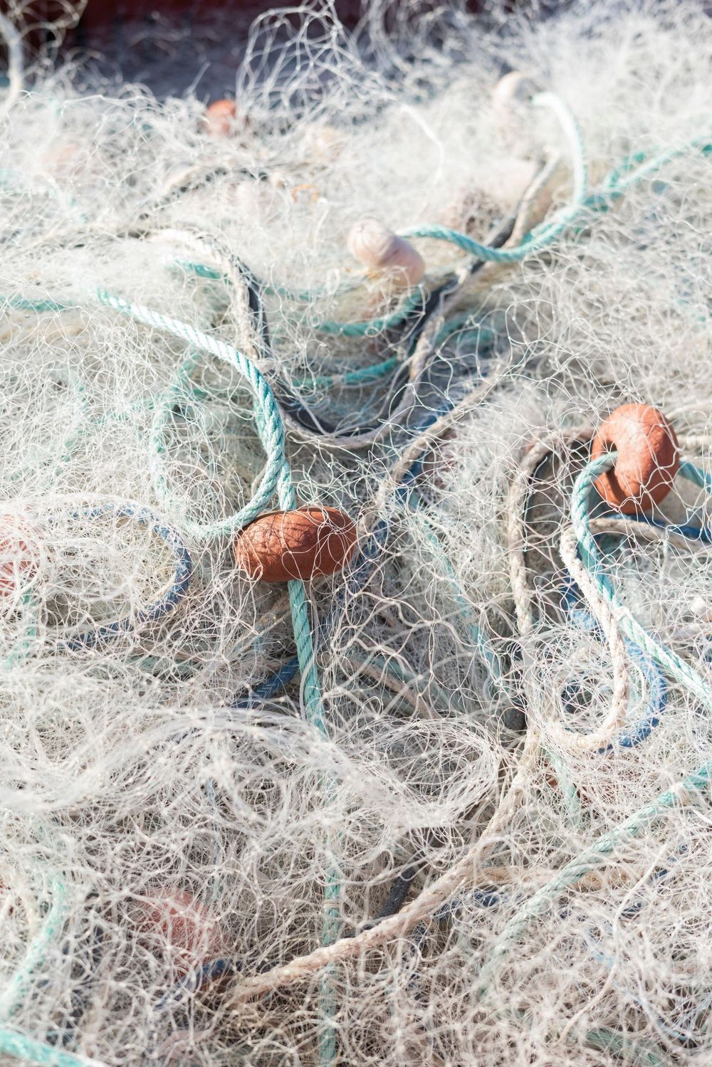 Old fishing net with caught cork floaters tangled in white mesh showing marine pollution and discarded gear.