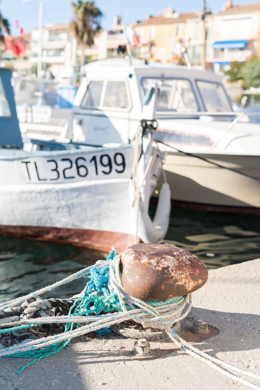 A rustic mooring with blue rope and fishing buoy at a marina with boats in the Mediterranean background.