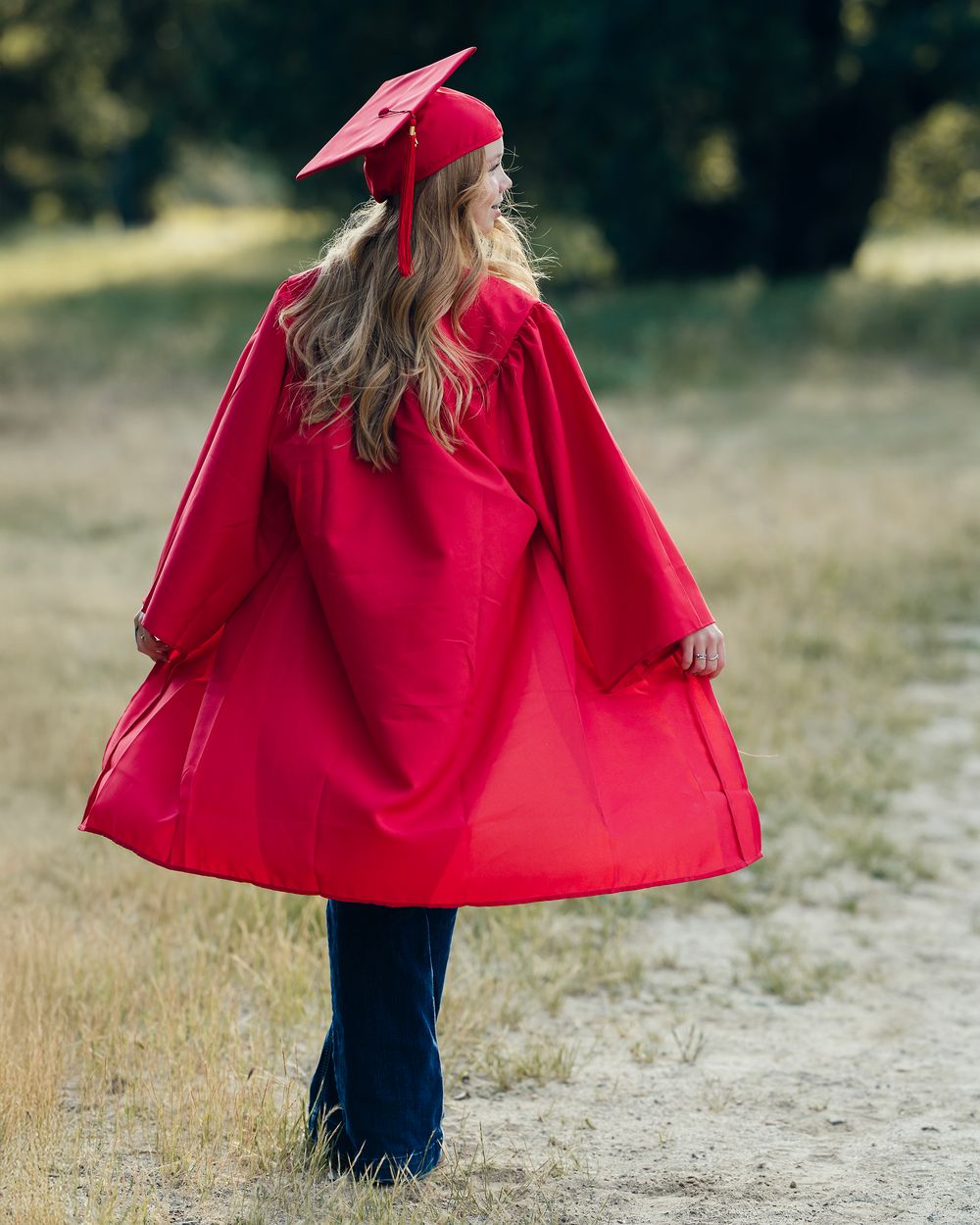 Red graduation gown and cap silhouetted against trees in golden afternoon light.