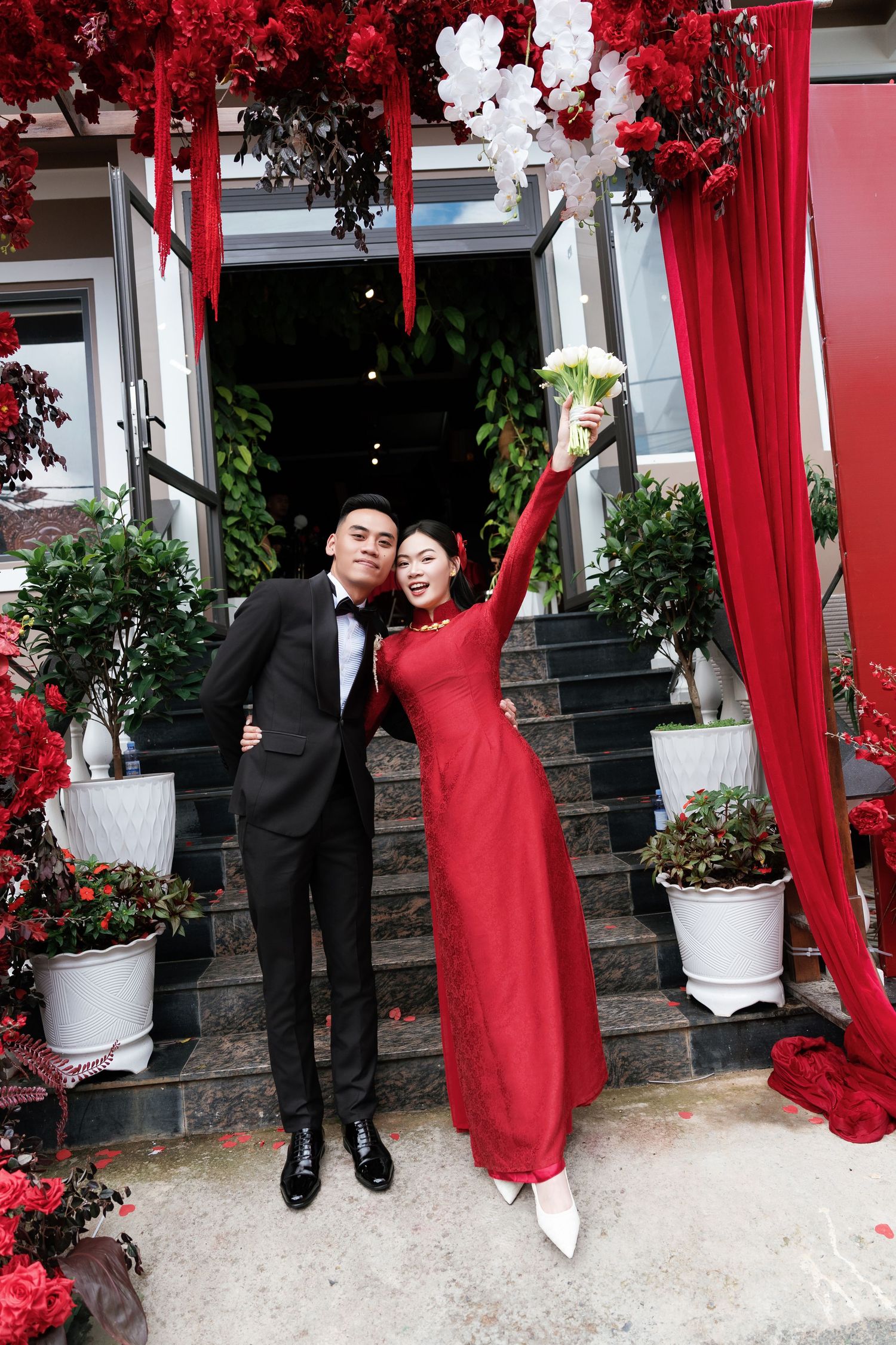 A romantic wedding moment with couple kissing under a white floral arch decorated with white roses and greenery.