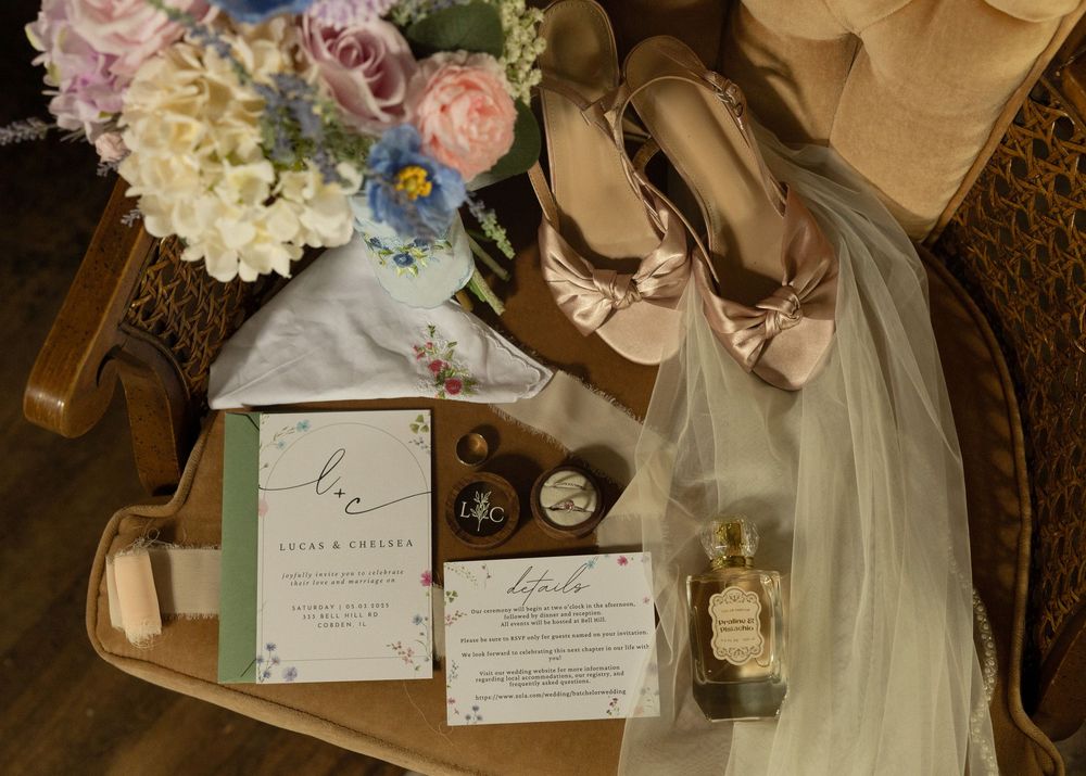 Wedding details including invitation, shoes, veil and floral bouquet arranged on wooden surface.