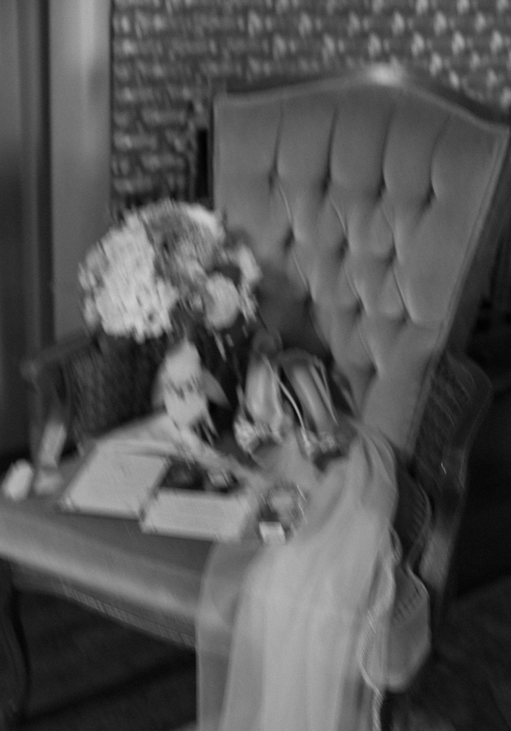 Black and white photo of wedding accessories on tufted chair.