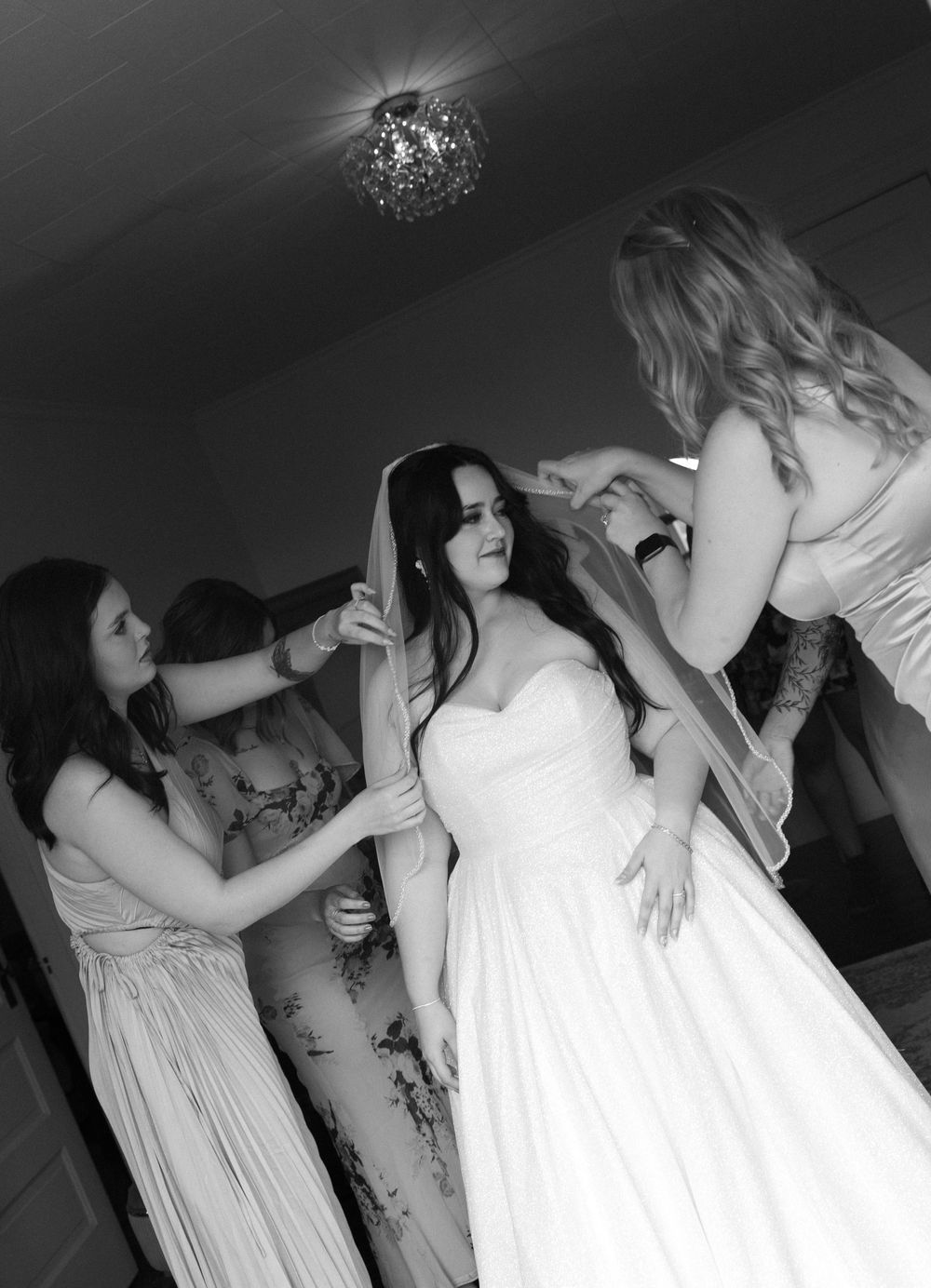 Black and white photo of wedding dress fitting with assistants helping.