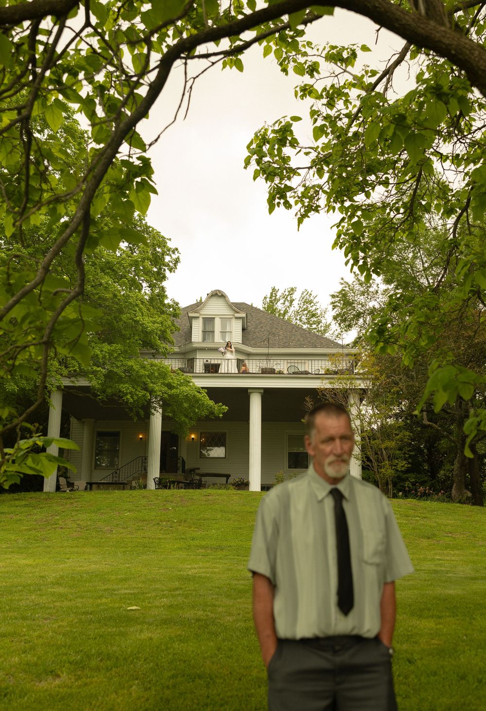 A stately white colonial house with a front porch and cupola photographed through green summer foliage.