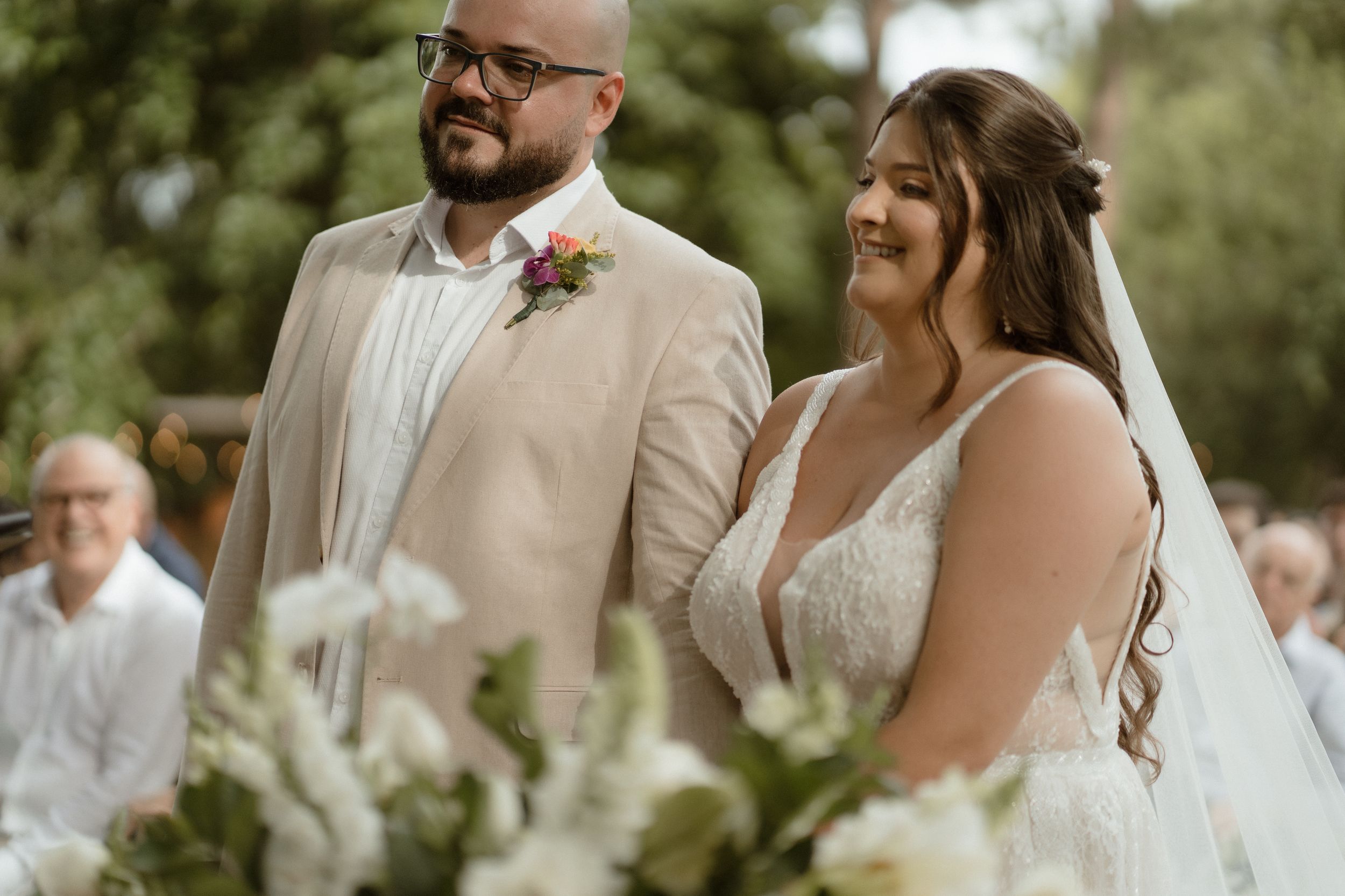 A joyful wedding ceremony moment under trees with white floral decorations.