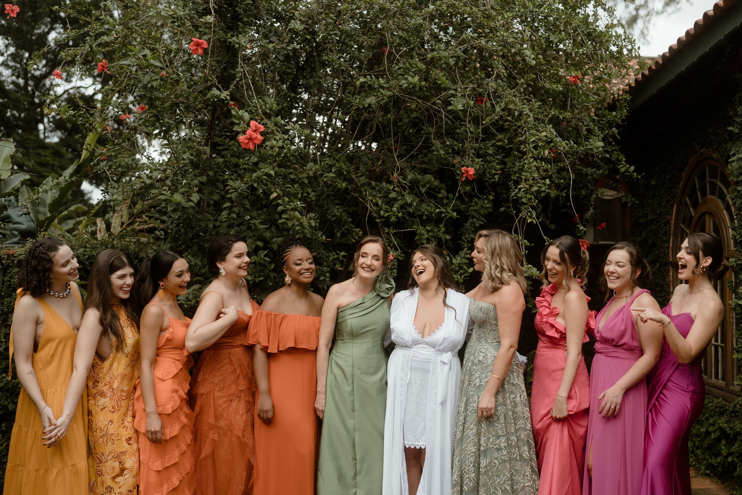 Wedding party wearing colorful dresses in orange, green, and pink tones standing together outdoors.