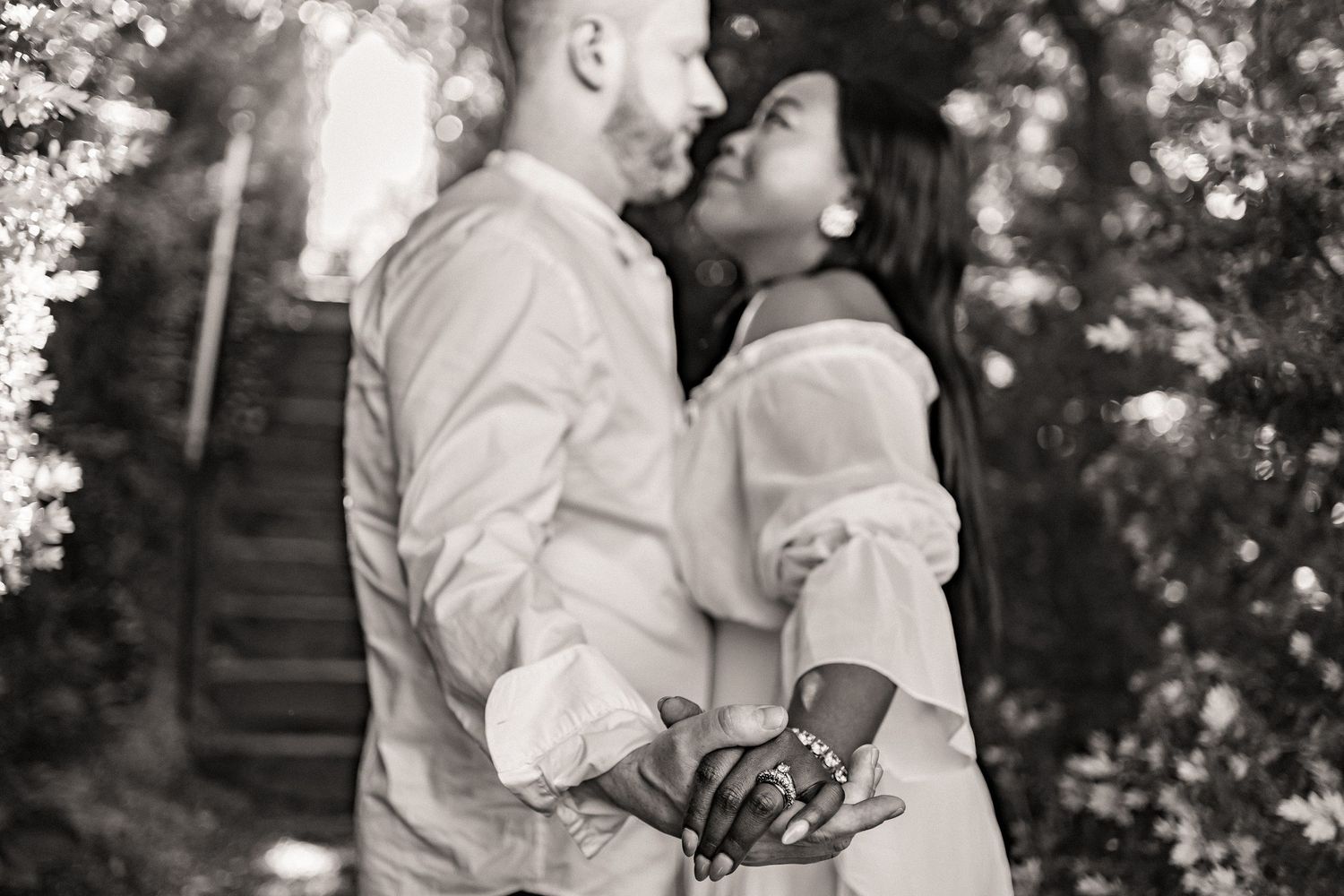 A romantic black and white photo of a tender embrace between two people in white clothing outdoors.