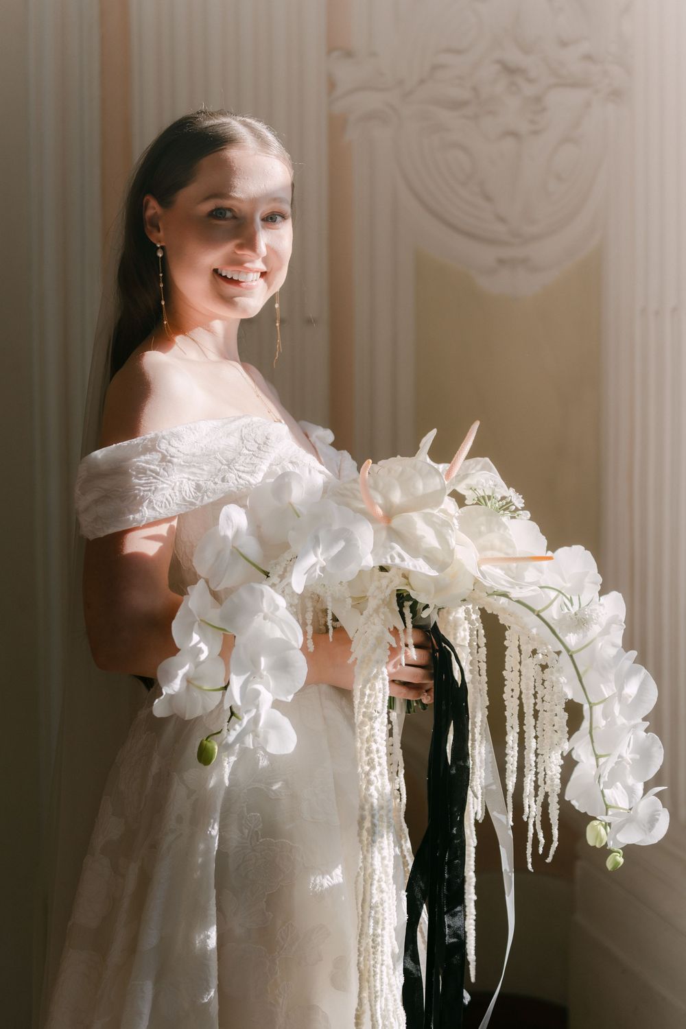 Beautiful wedding portrait showing off-shoulder dress and elegant white orchid bouquet with cascading ribbons in natural light.
