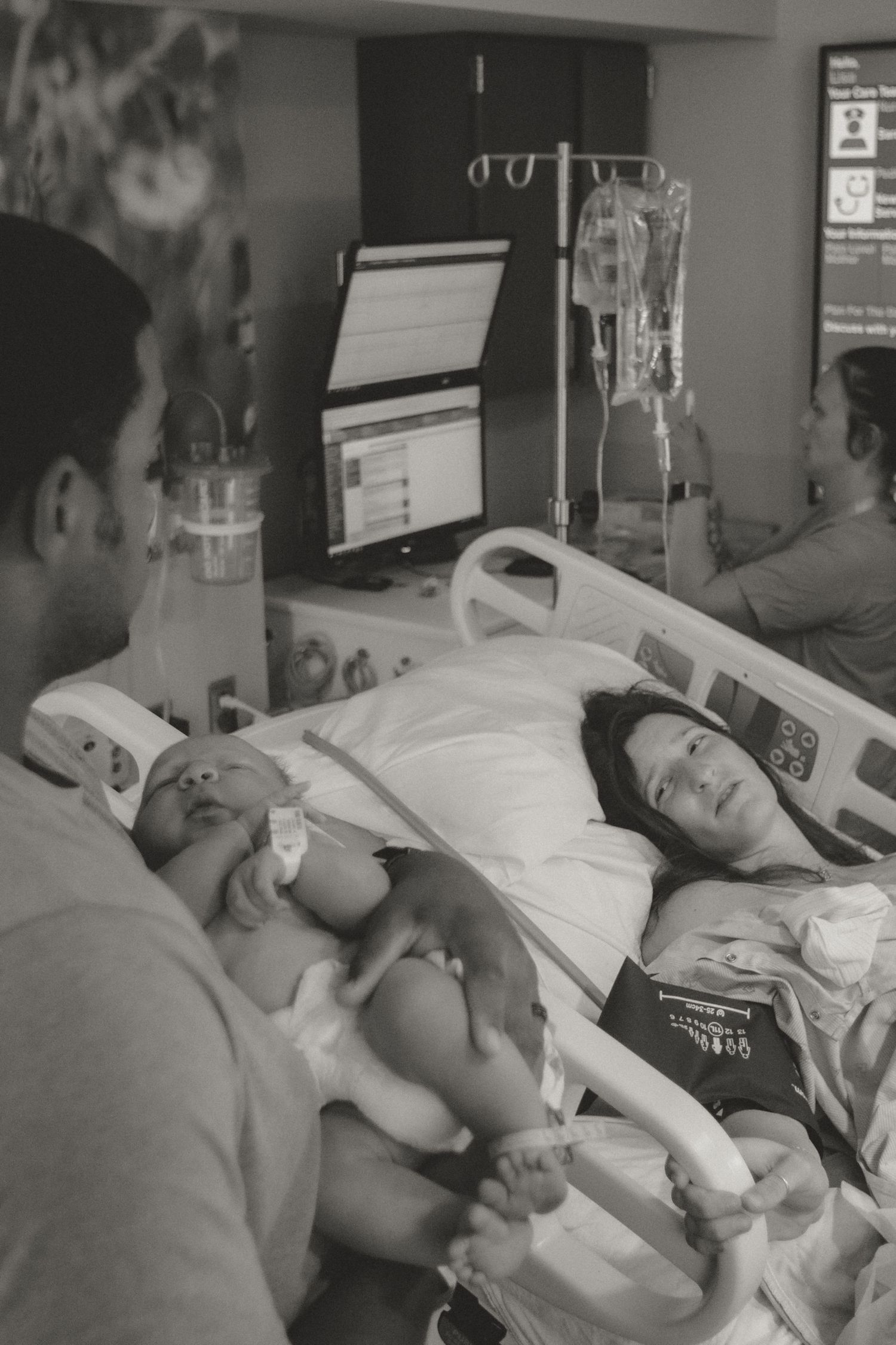 Hospital room scene with medical equipment and monitors as a family bonds with their newborn baby.