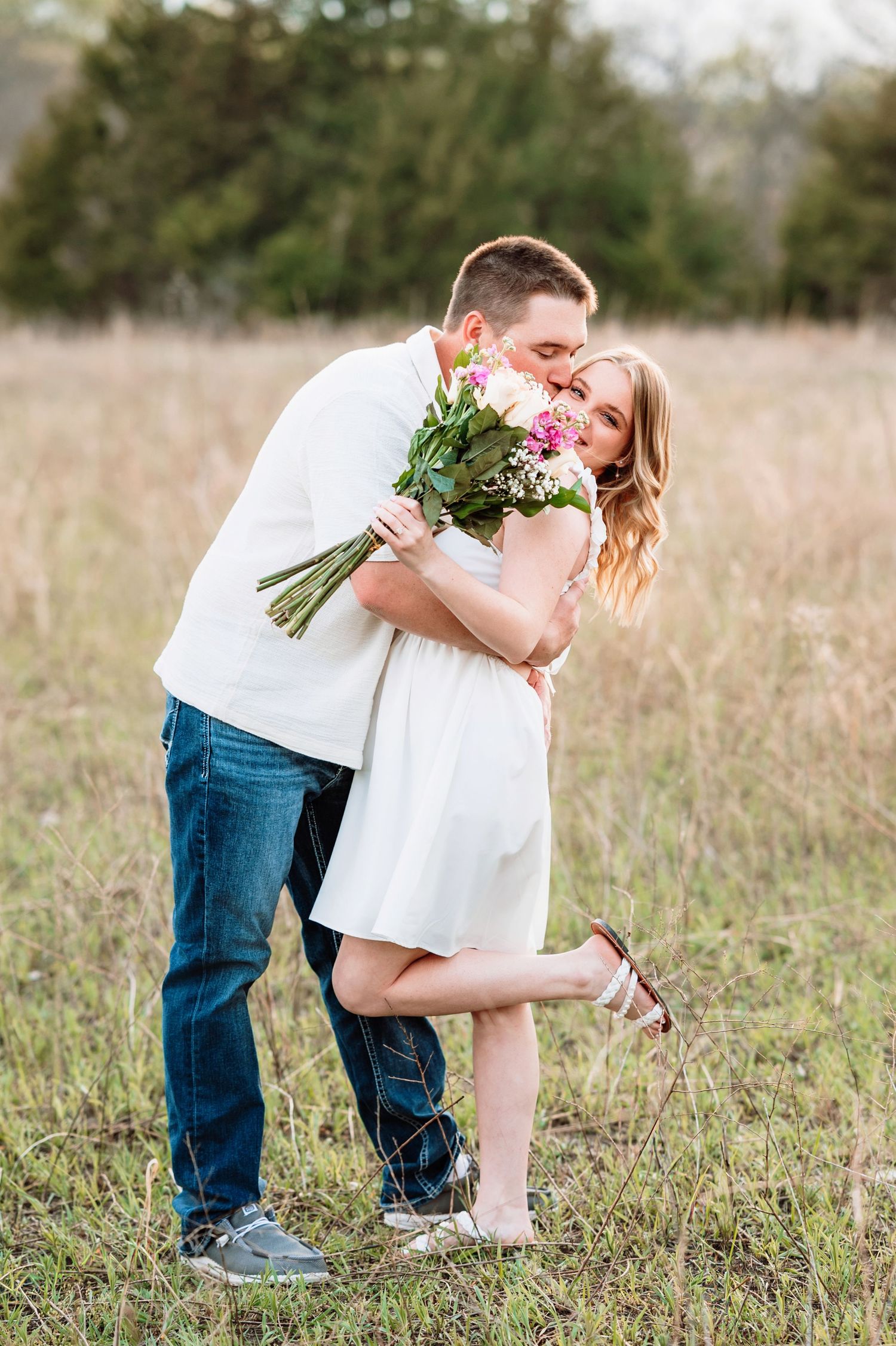 A couple shares a romantic moment in a golden field while holding a bouquet of fresh flowers.
