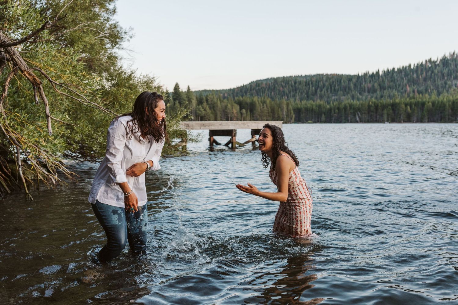 Two people playing and splashing in a mountain lake surrounded by trees.