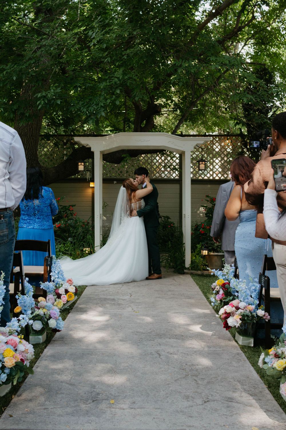 A sequence of wedding photos showing a bride and groom dancing under a white lattice pergola with colorful floral decorations.
