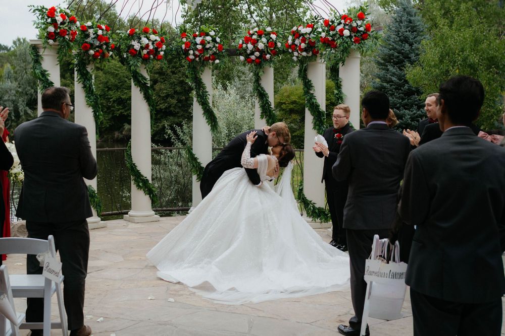A wedding ceremony takes place outdoors under white pergolas with guests watching the couple exchange vows.