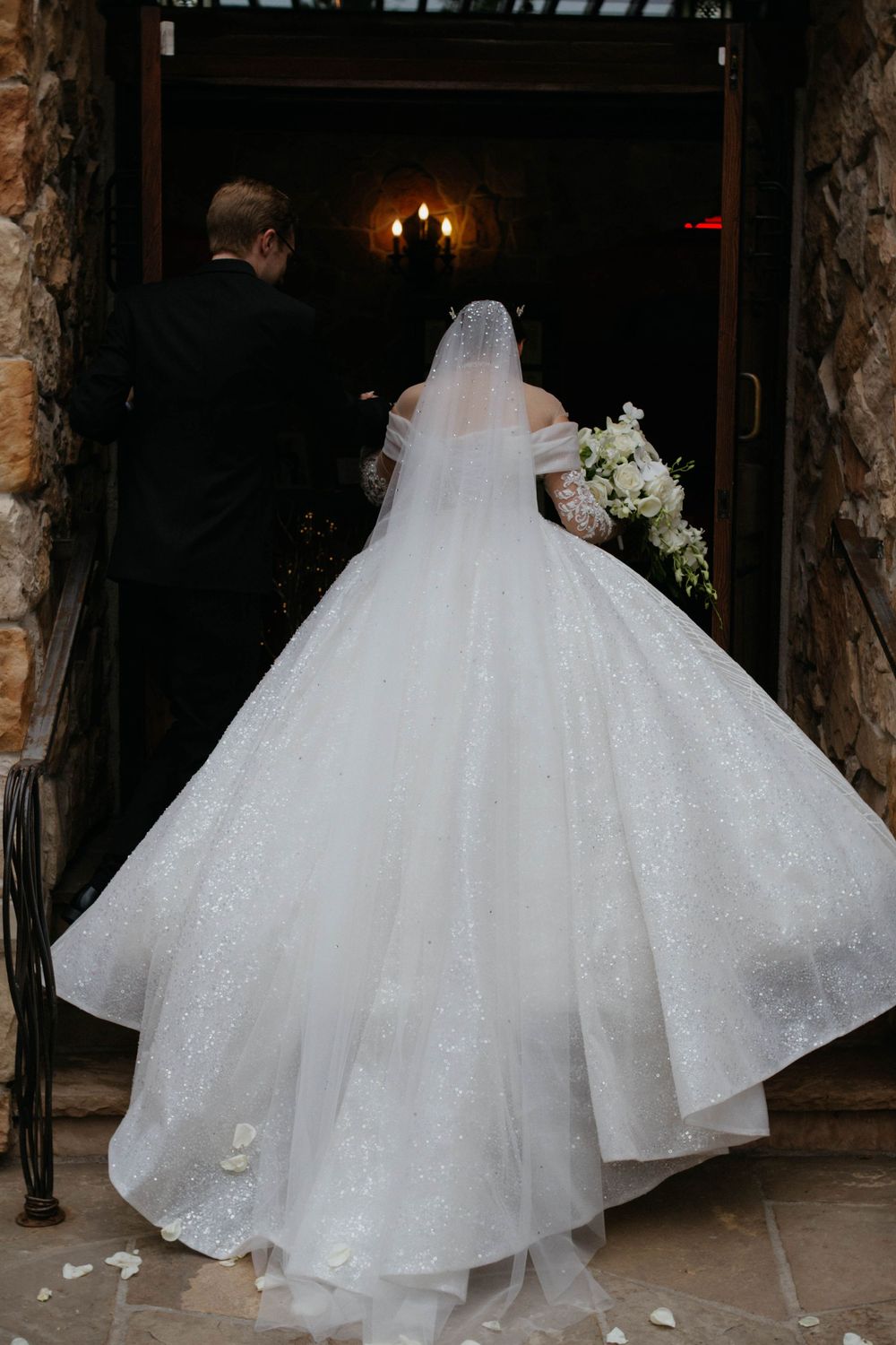 A bride in a flowing white ball gown with a cathedral train walks through a dimly lit venue during her wedding.