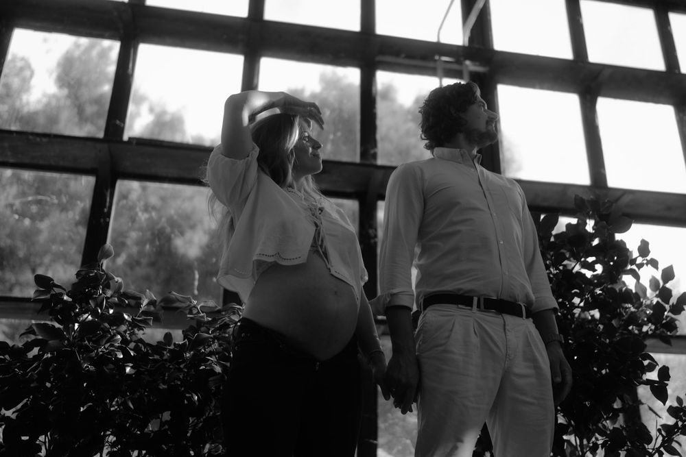Silhouettes of a couple stand together by large windows in a romantic indoor setting.