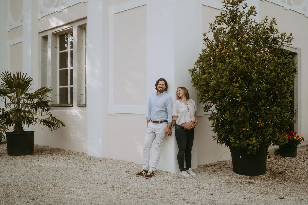 A couple walks hand in hand along a white building exterior with potted plants.