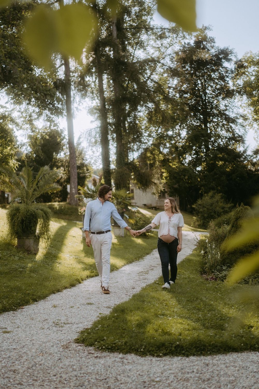 A couple strolls together on a winding gravel path surrounded by lush greenery.