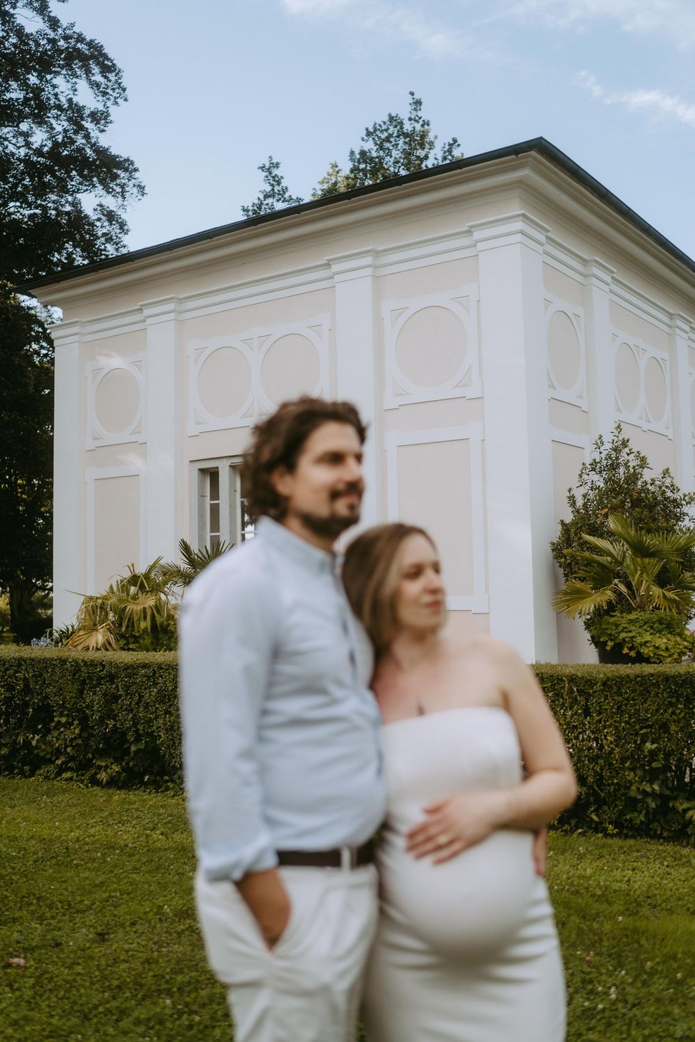 A couple embraces in front of a classic white building with architectural details.