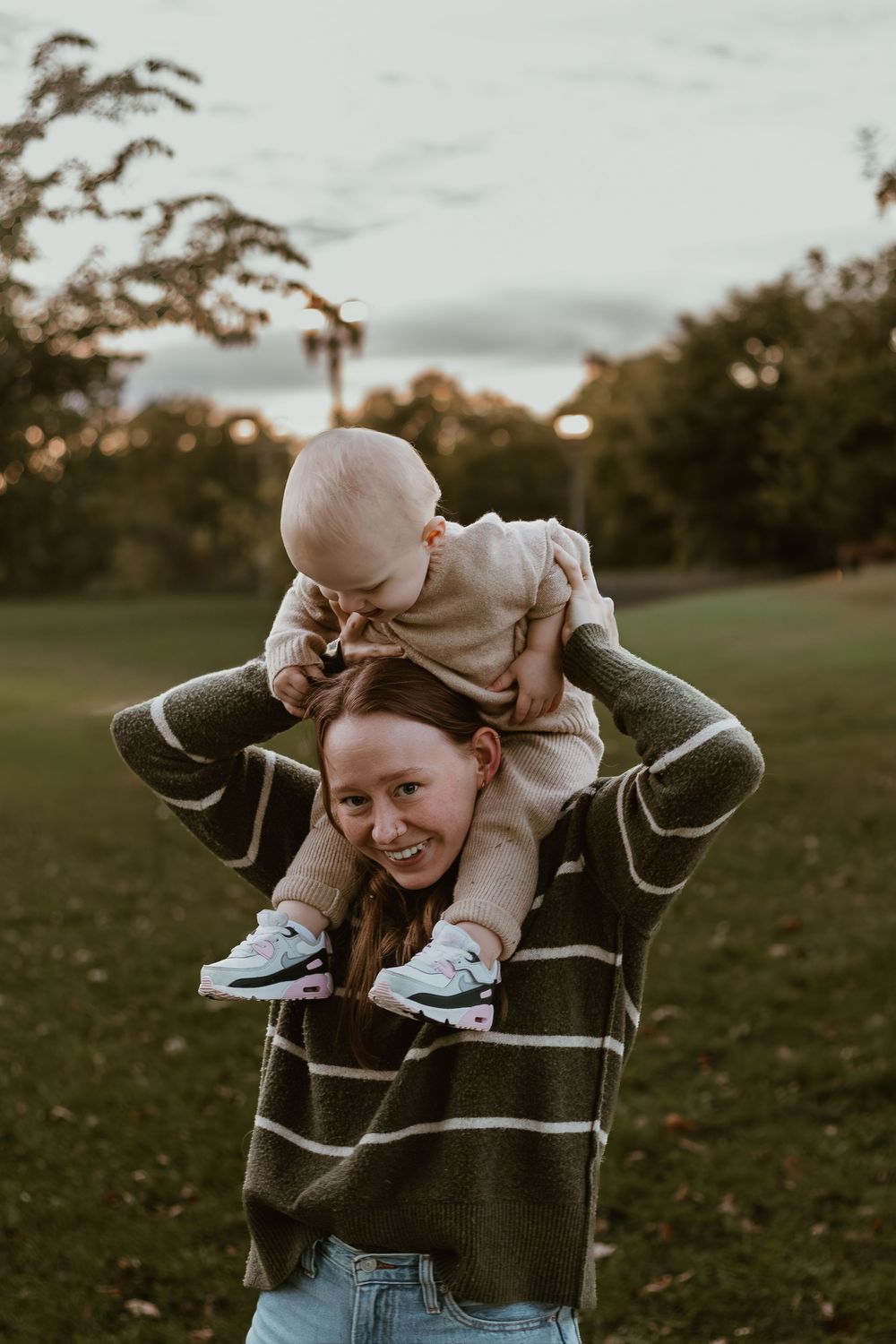 A playful sequence of someone wearing a striped sweater holding and swinging a baby in an outdoor field at sunset.