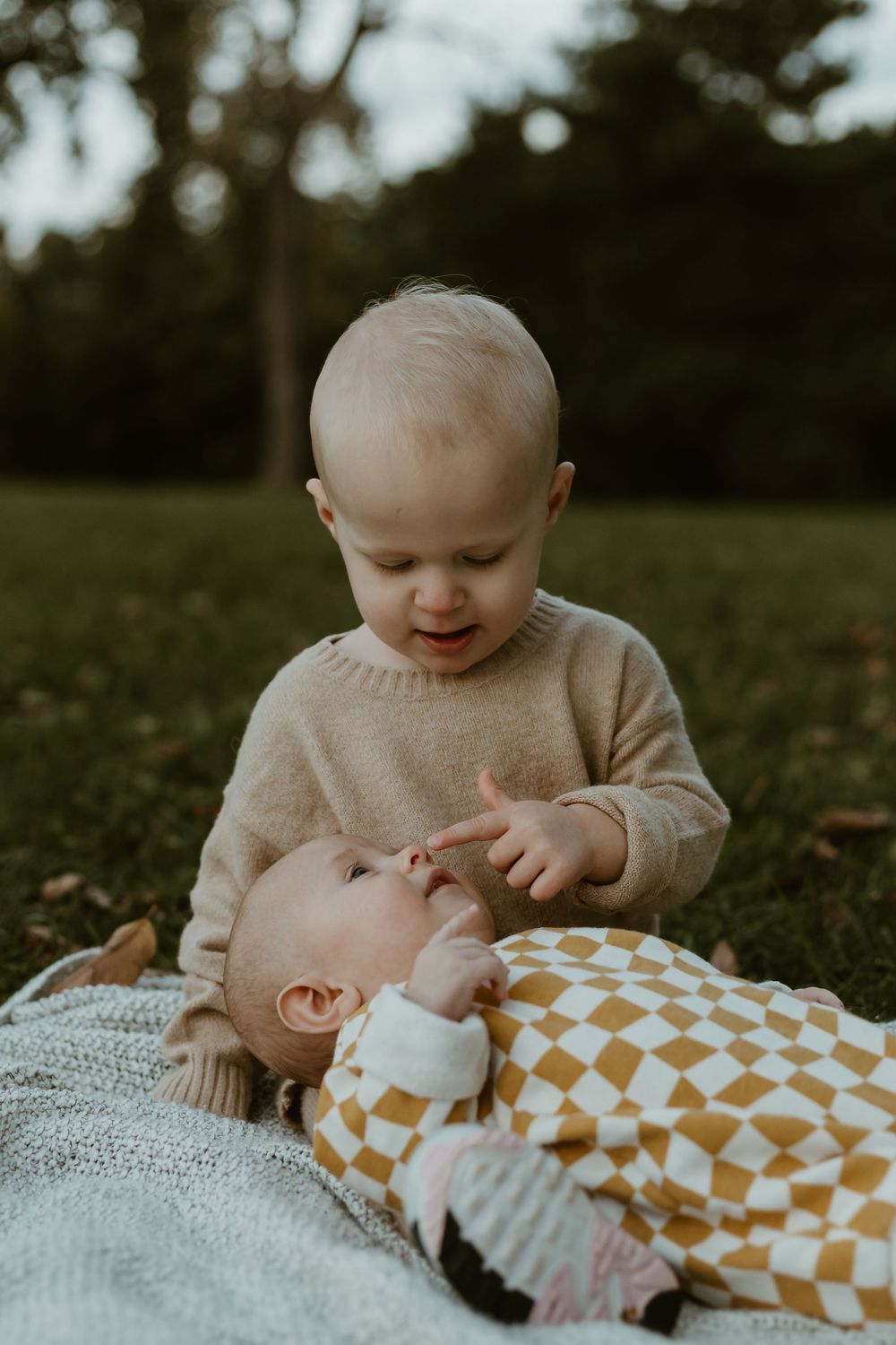 Two small children share a tender moment while laying on a blanket outdoors.