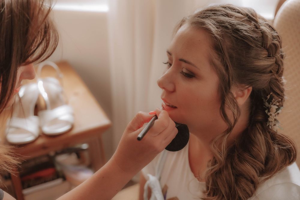 A series of wedding preparation photos showing makeup application and hair styling in a bright, elegant setting.