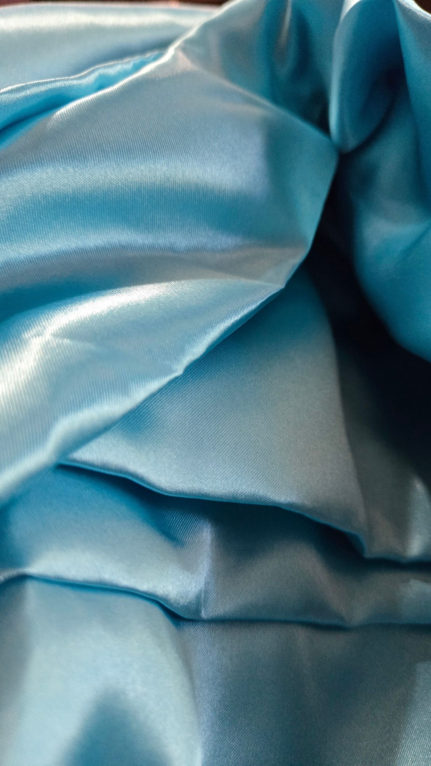 Close-up view of shiny turquoise blue satin fabric with gentle folds and creases creating a luxurious texture.