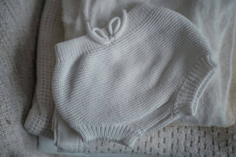 Neutral baby clothing stacked gently for an in-home newborn lifestyle photoshoot in Derbyshire, capturing soft textures and natural light.