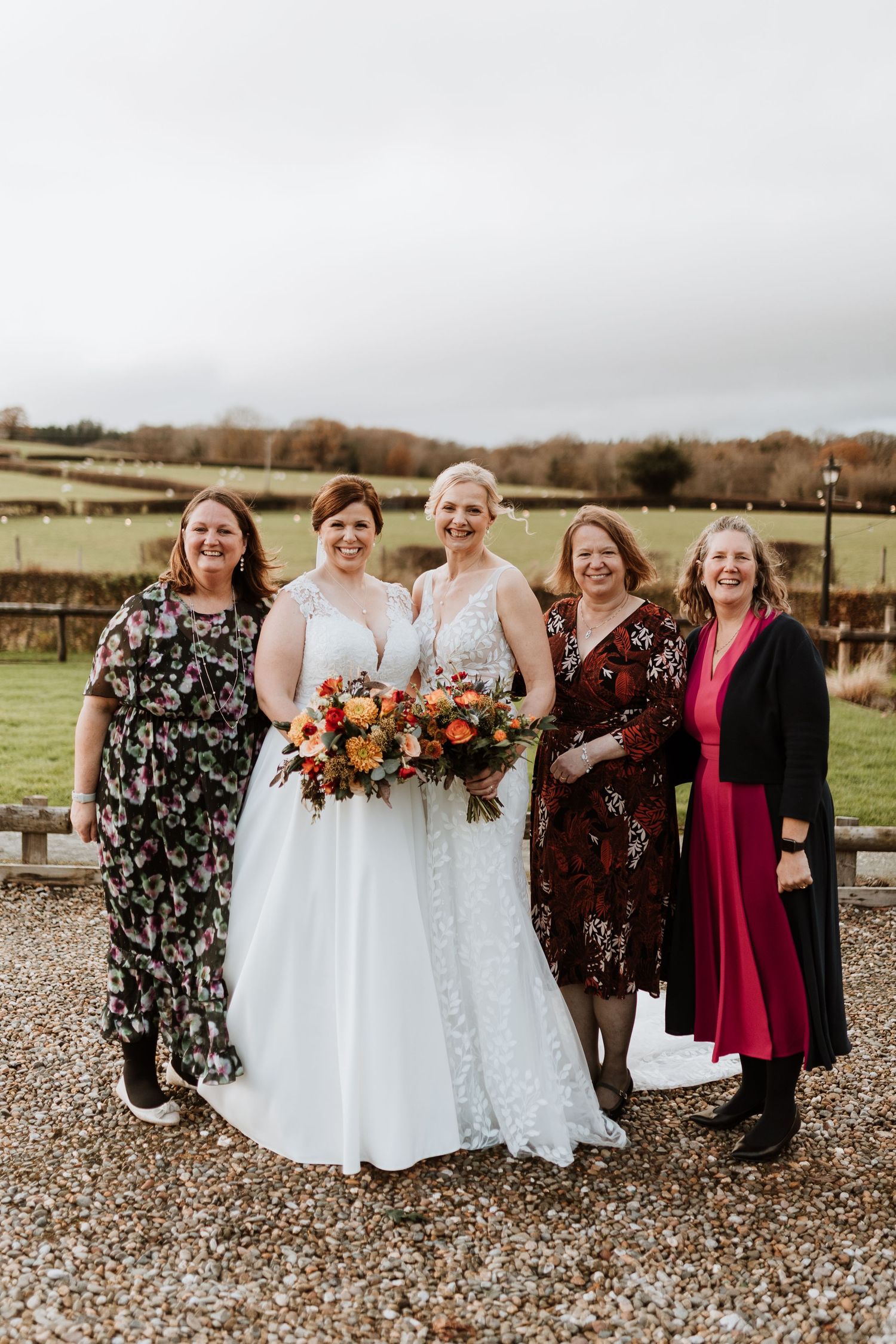 A group in formal attire poses together outdoors on a gravel path with autumn fields in the background at Tower Hill Barns.