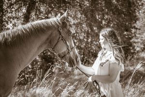 A black and white photo of a horse and rider walking through a scenic wooded trail in dappled sunlight.