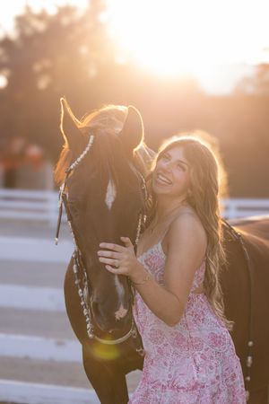 A woman shares a tender moment with her horse in warm evening sunlight while wearing a pink dress.