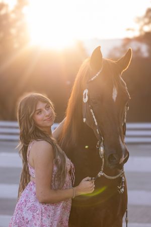 Woman in pink floral dress shares tender moment with dark horse at sunset.