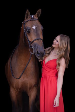A bay horse and person in a red dress pose together against a dark background.