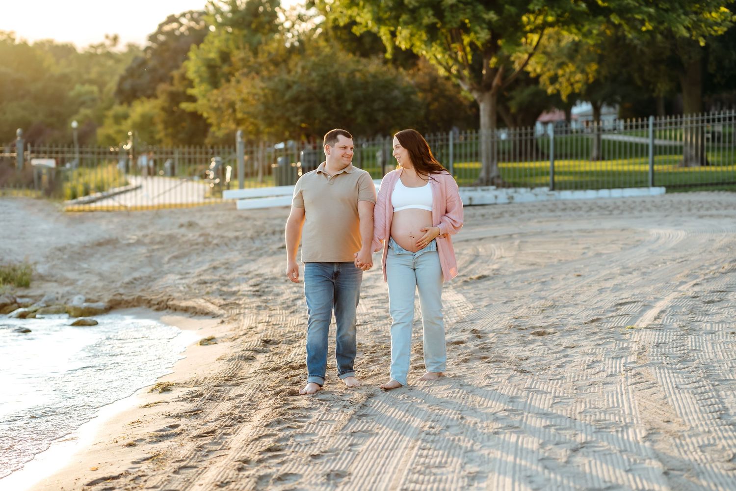 Couple walking together on sandy beach at sunset with warm golden light filtering through trees.