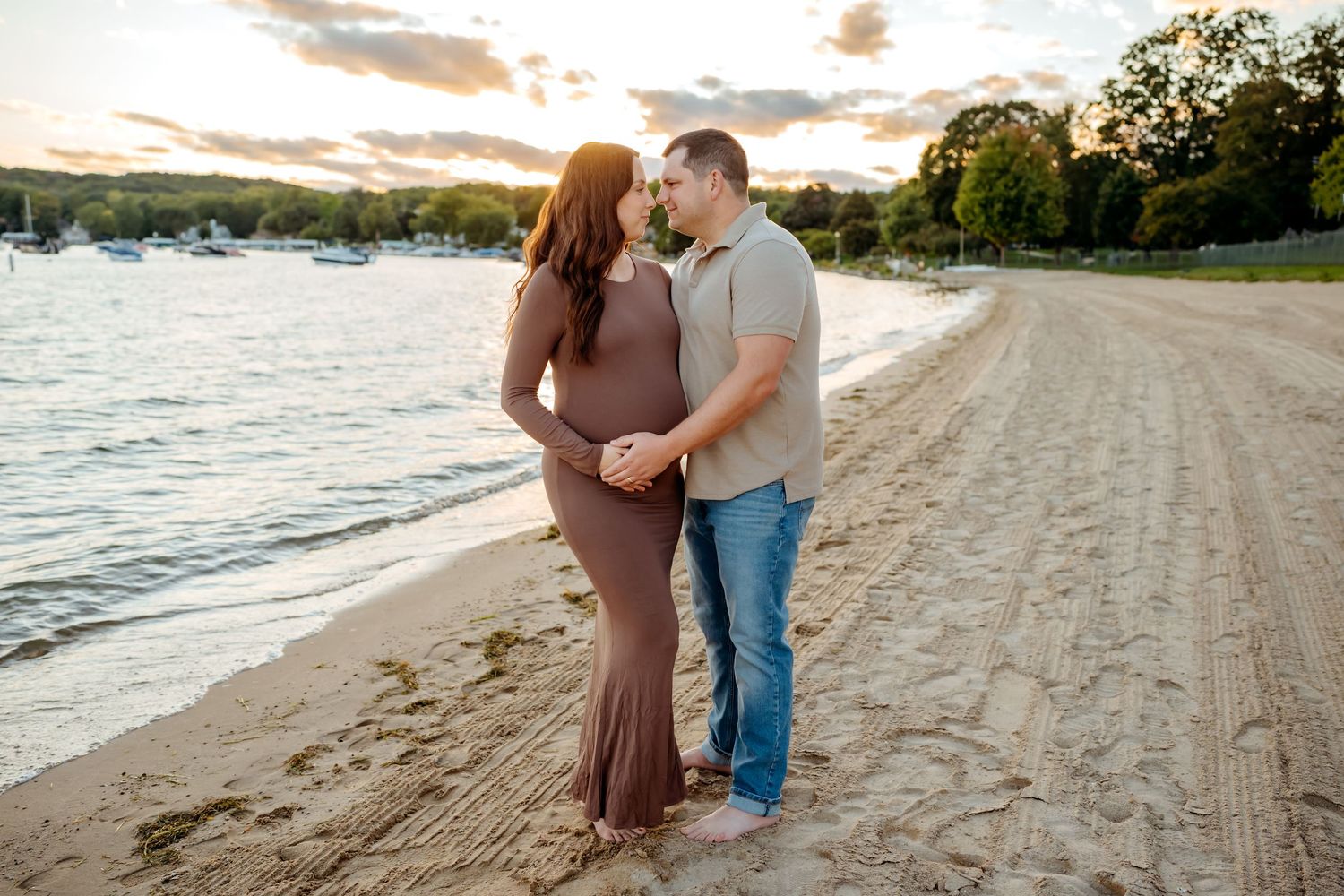 A couple in casual attire shares a romantic moment on a sandy beach at sunset.