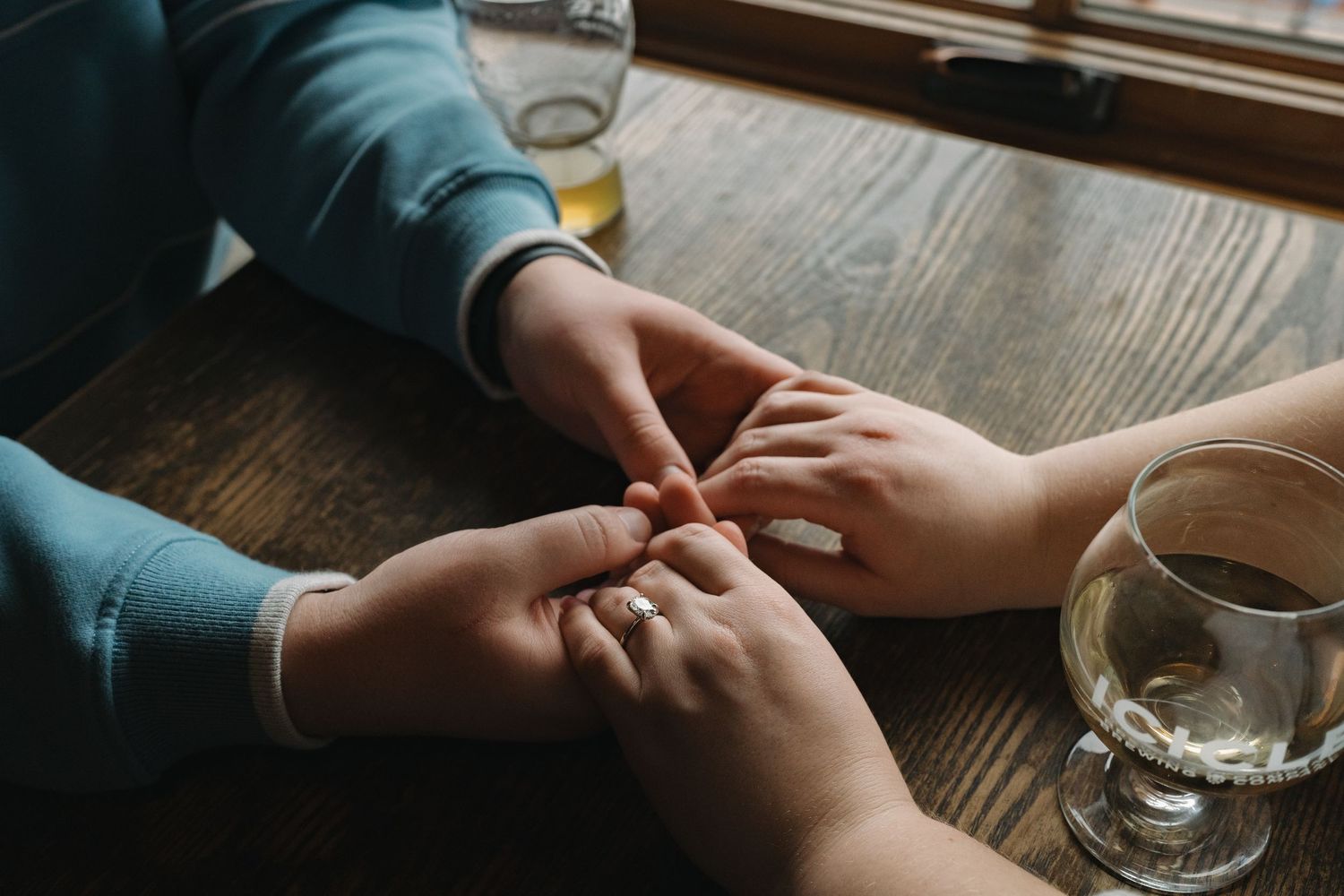 Two people hold hands across a wooden table in a restaurant setting, showing an intimate moment of connection. Leavenworth, WA