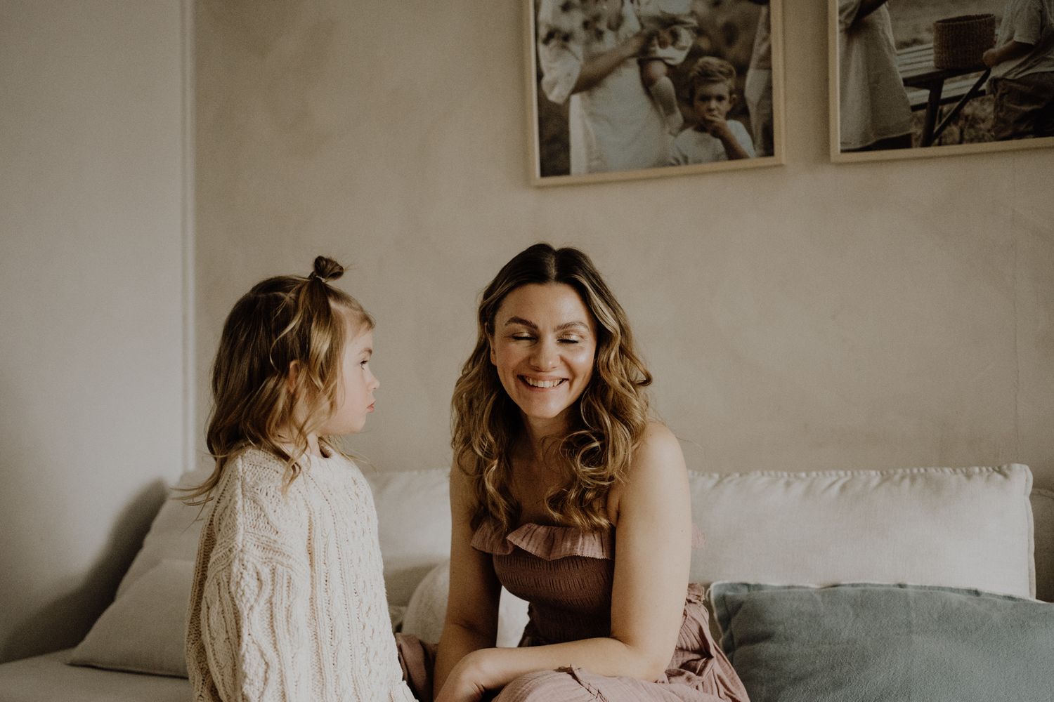 A tender moment captured in warm sepia tones as mother and daughter share loving interactions on a couch.