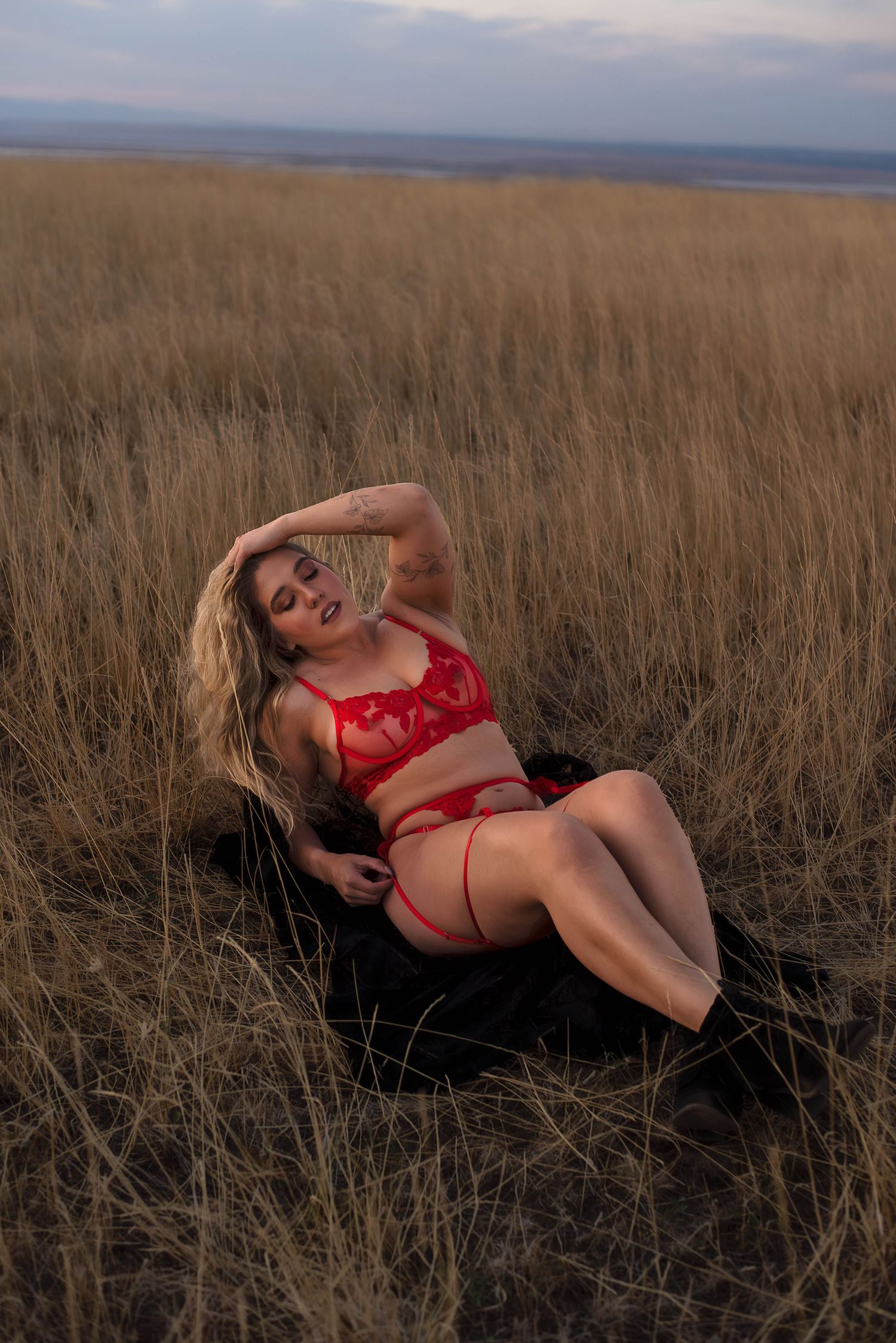 Boudoir photography of a woman laying in a field in red lingerie enjoying the sun on her body in Utah