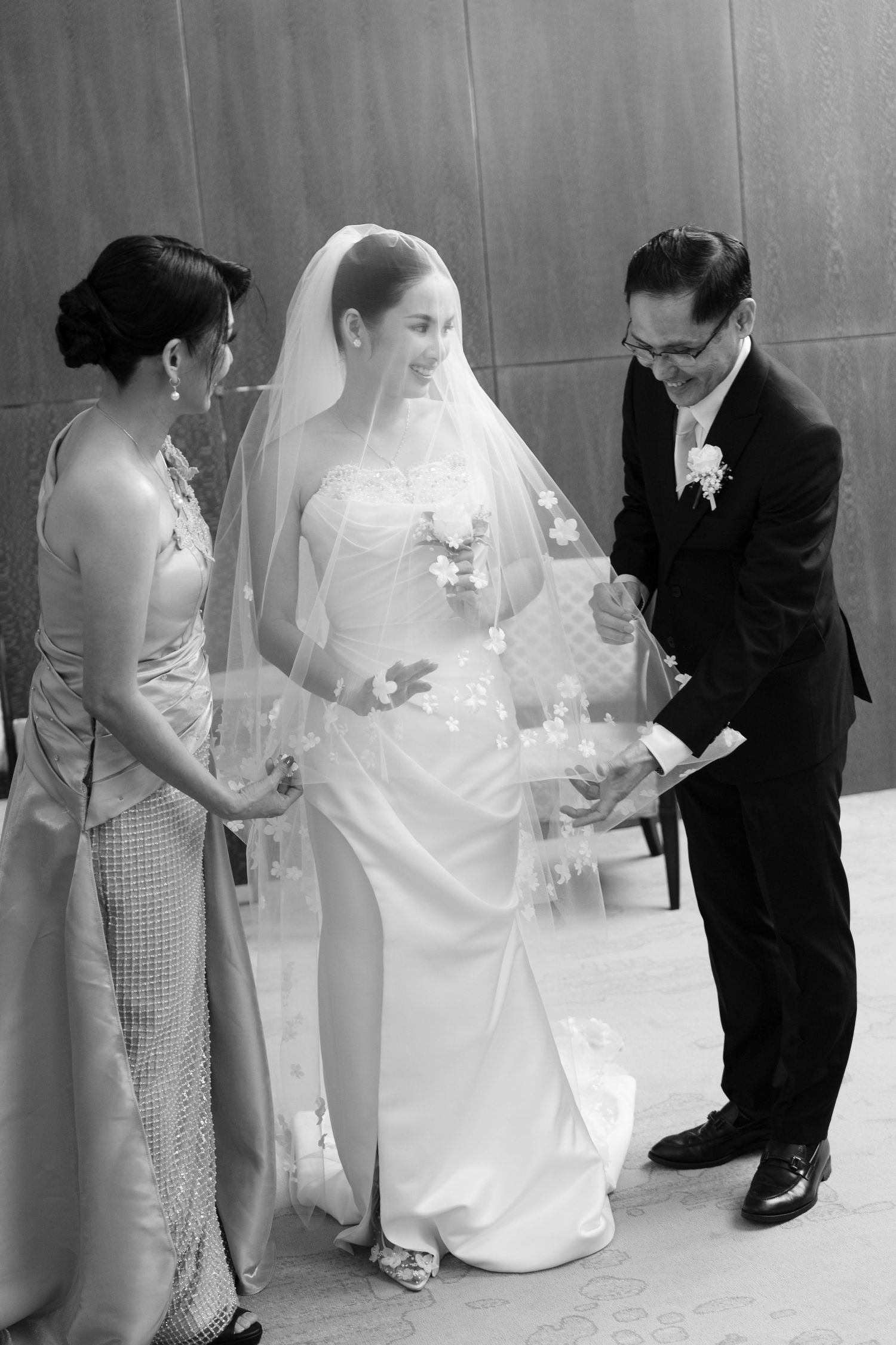Black and white photo of bride with parents adjusting her veil before the wedding ceremony.