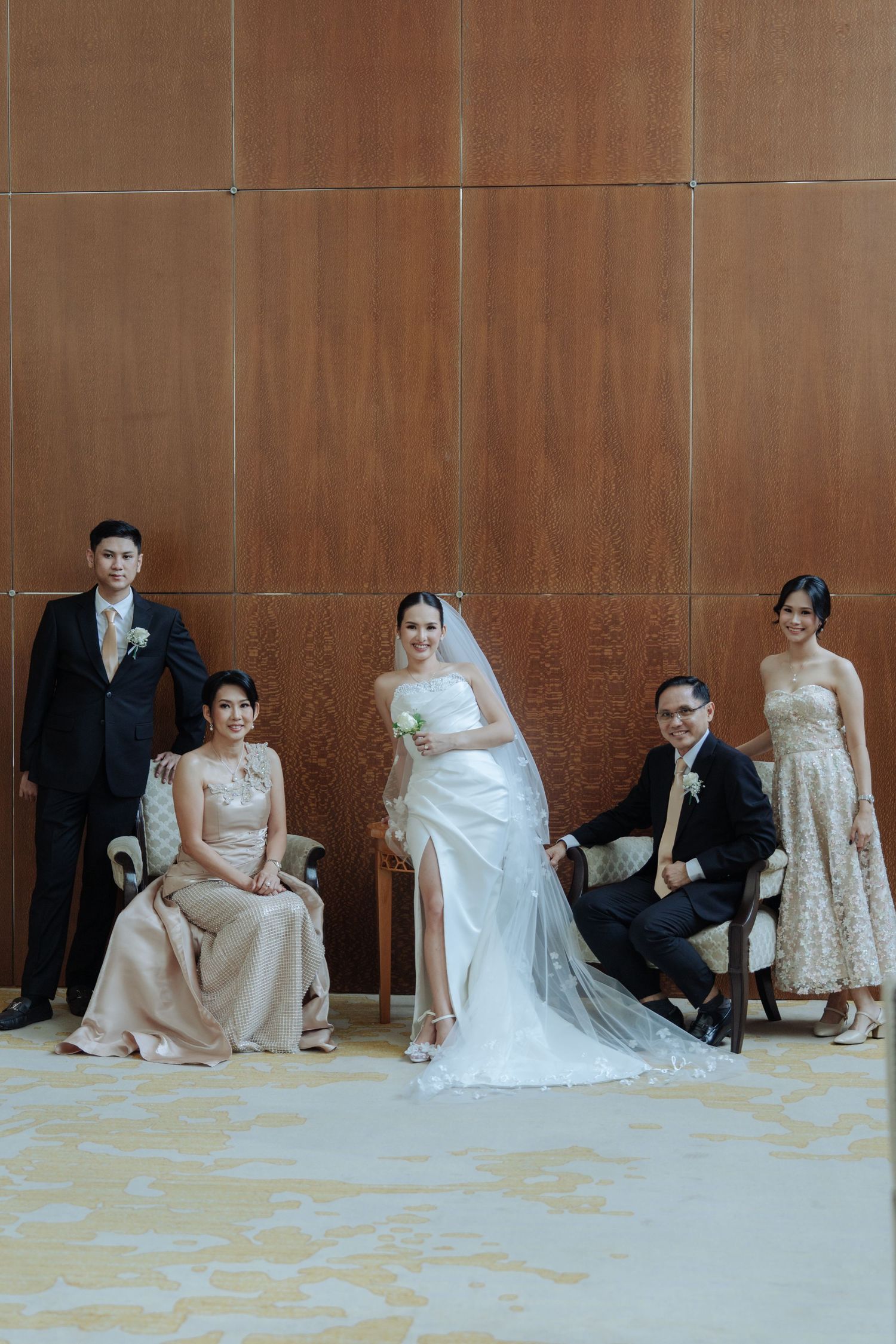 Bride in white gown poses with family of five against a wooden wall in elegant venue.