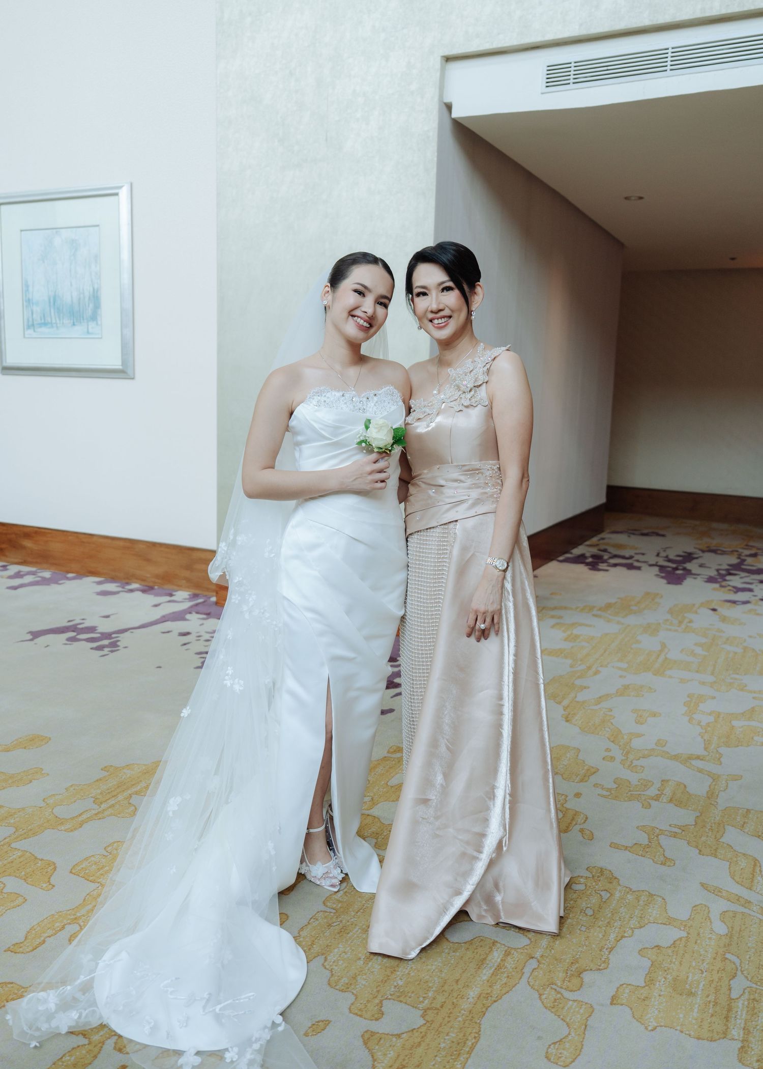 Bride in white gown holds bouquet while posing with bridesmaid in champagne dress at indoor wedding venue.